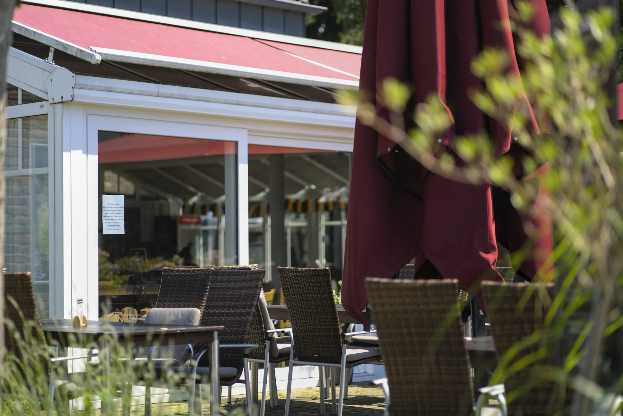 Die sonnige Terrasse des Treff.clubhaus2 am Golfclub Niep mit roten Sonnenschirmen